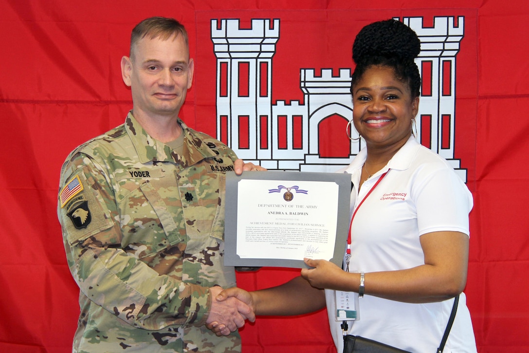 An army colonel hands a certificate to a person and shakes her hand.