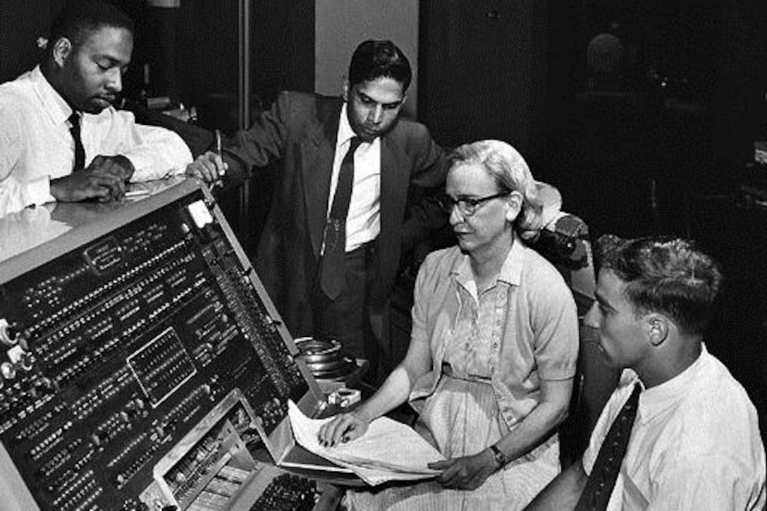 A woman programmer sits with others near a computer.