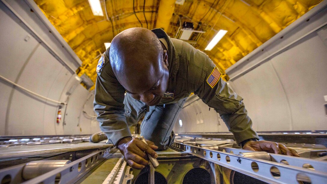 An airman on his hands and knees inspects an aircraft's interior with a flashlight.