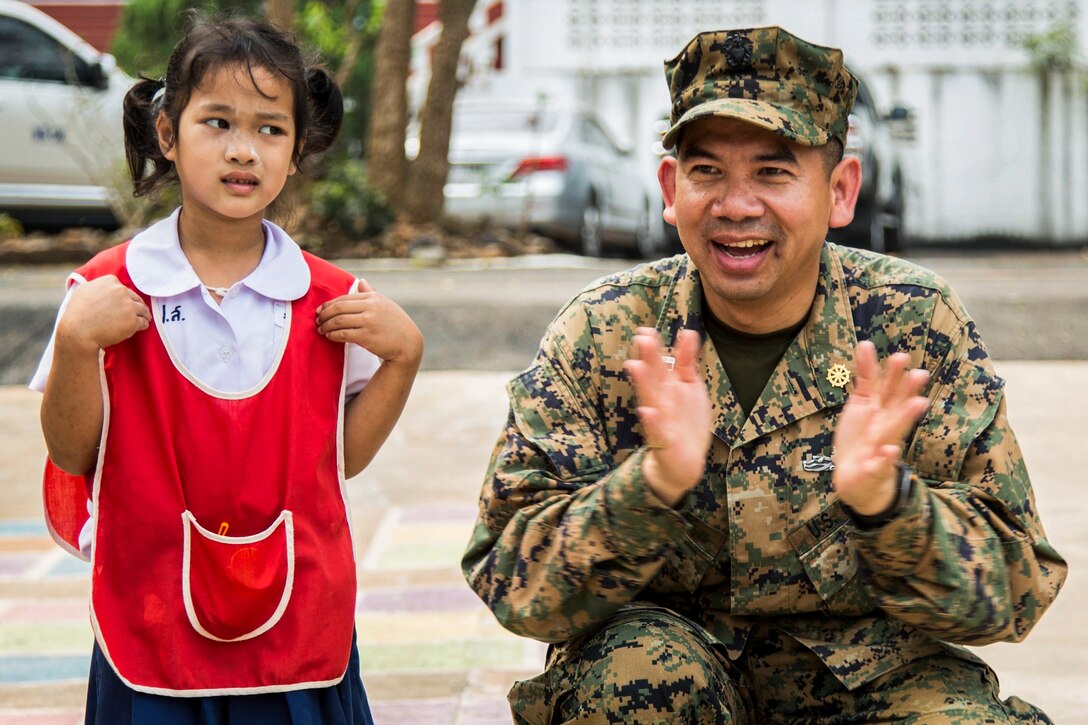 A girl with her fingers under her armpits gives a sidelong glance as a smiling sailor crouching next to her claps.