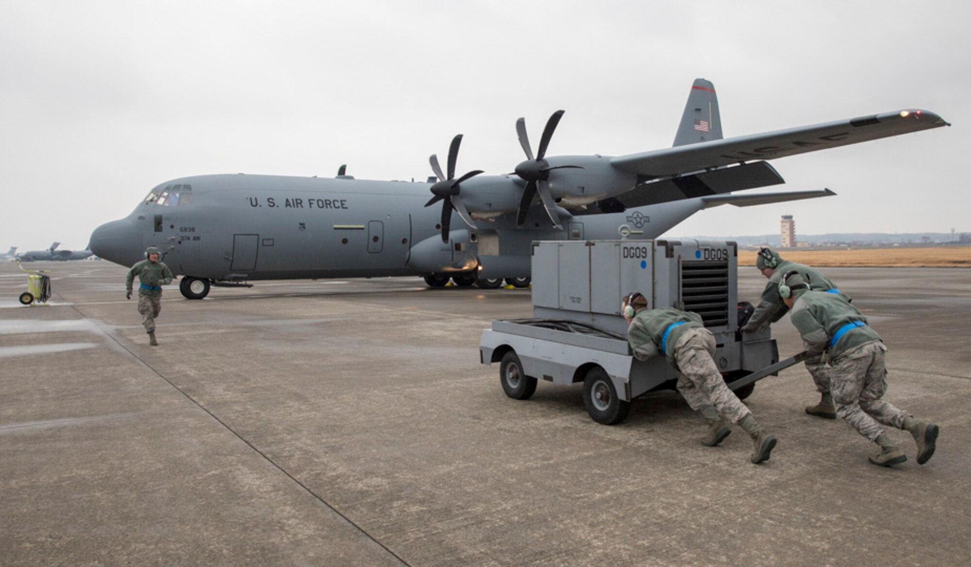 Airmen from the 374th Aircraft Maintenance Squadron push an A/M32 diesel generator to a waiting C-130J Super Hercules assigned to the 36th Airlift Squadron