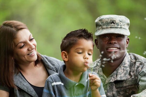 A boy blows spores from a dandelion while sitting between his parents.