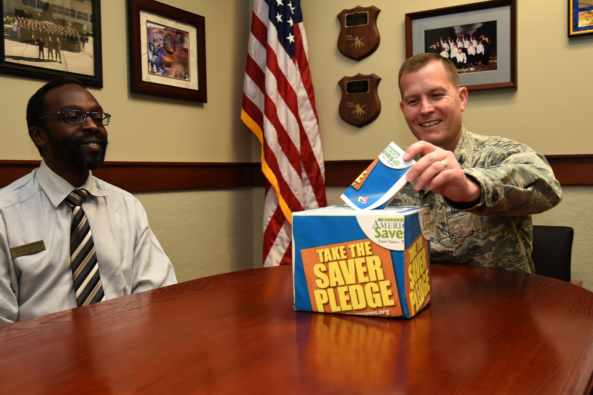 Financial Readiness manager, William Gathecha watches as U.S. Air Force Col. Jeffrey Sorrell, 17th Training Wing vice commander, folds his pledge slip to go into the saver pledge box at the Norma Brown building on Goodfellow Air Force Base, Texas, on Feb. 23, 2018. This box is one of several ways individuals can commit to a savings plan in addition to attending classes the Airman and Family Readiness Center will be hosting Feb. 26 through March 3. (U.S. Air Force photo by Airman 1st Class Seraiah Hines/Released)