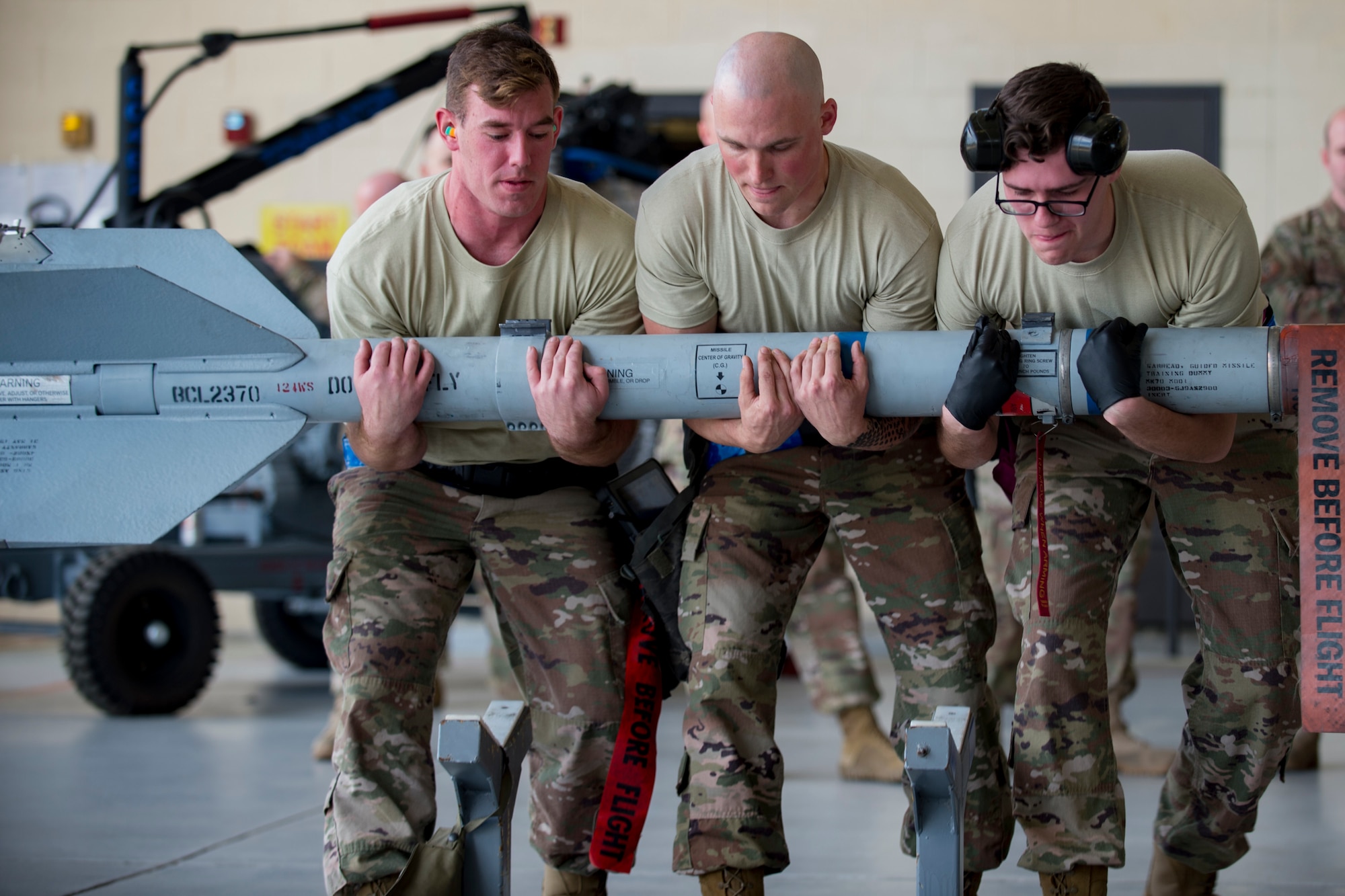 Airman 1st Class Hunter Leger, left, Staff Sgt. Ryan Amos, center, and Airman 1st Class Joseph Capshaw, right, all 74th Aircraft Maintenance Unit (AMU) weapons-load crewmembers, lift an inert AIM-9 air-to-air missile during a weapons-load competition, Feb. 22, 2018 at Moody Air Force Base, Ga. Judges assessed the 75th and 74th AMUs on how quickly and efficiently they loaded munitions onto an A-10C Thunderbolt II during the loading portion of the competition. They were also judged on dress and appearance and a written test based on munition knowledge. (U.S. Air Force photo by Senior Airman Daniel Snider)