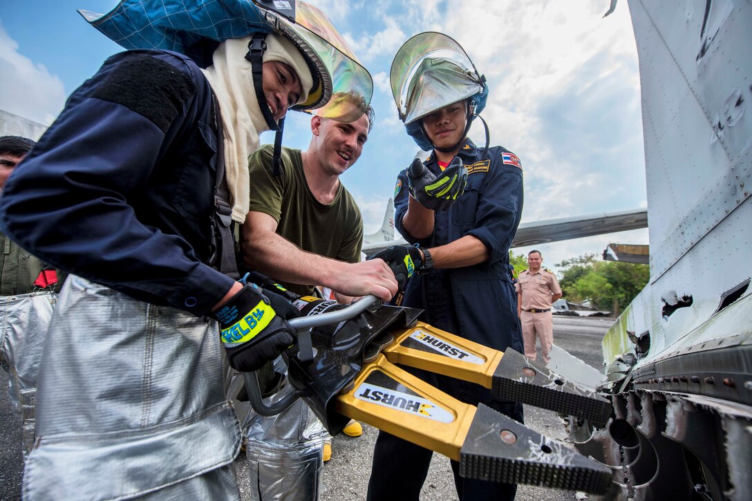 U.S. Marine Corps Sgt. Stanley Makinen, center, helps Thai navy Petty Officer 1st Class Pookan Phichakhorn, left, and Thai navy Petty Officer 2nd Class Kradkong Theerapat operate a hydraulic extractor.