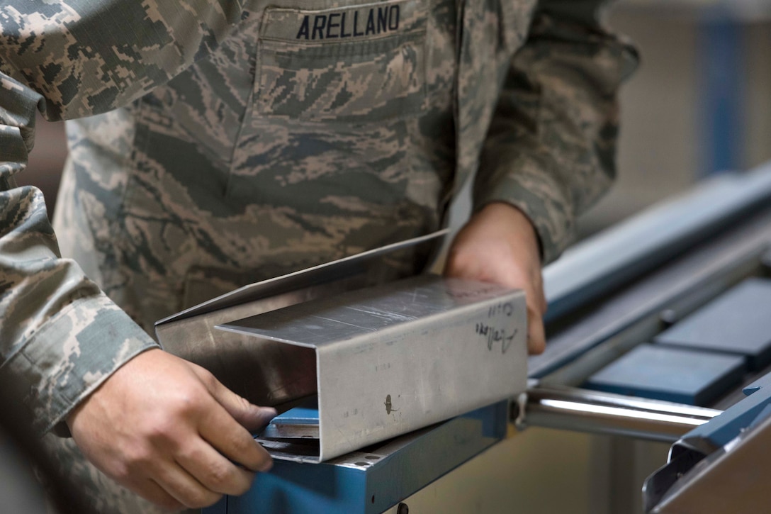 Air Force Airman Daniel Arellano adjusts sheet metal using a magnetic bending machine.