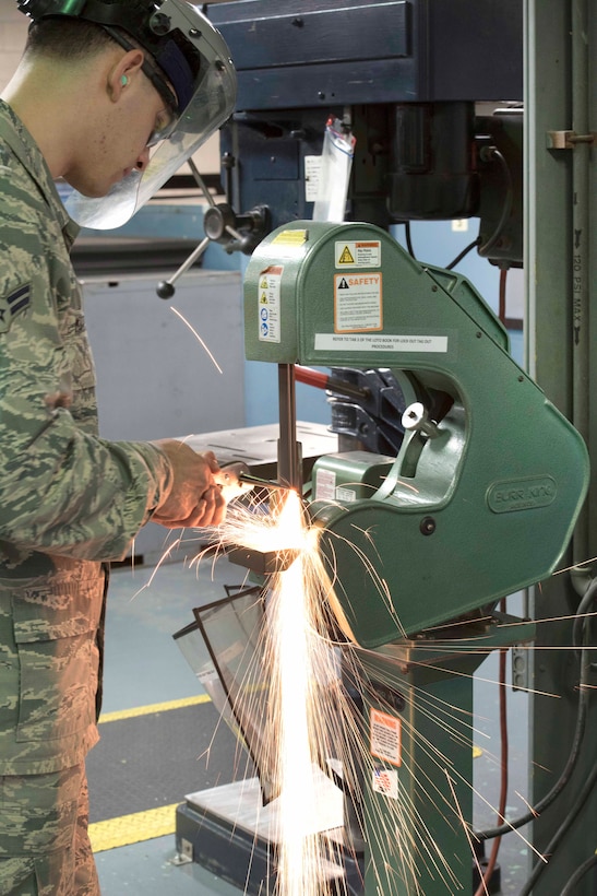 Air Force Airman 1st Class Gilbert Martinez sands down a piece of sheet metal using a belt sander.