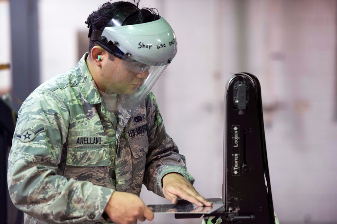 Air Force Airman Daniel Arellano sands a piece of sheet metal using a belt sander.