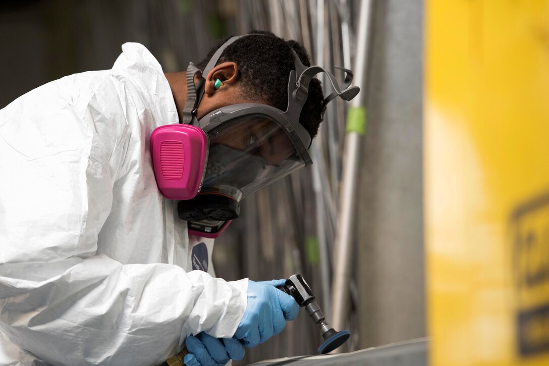 Air Force Airman 1st Class Jahmal Camp sands paint off from an adapter.