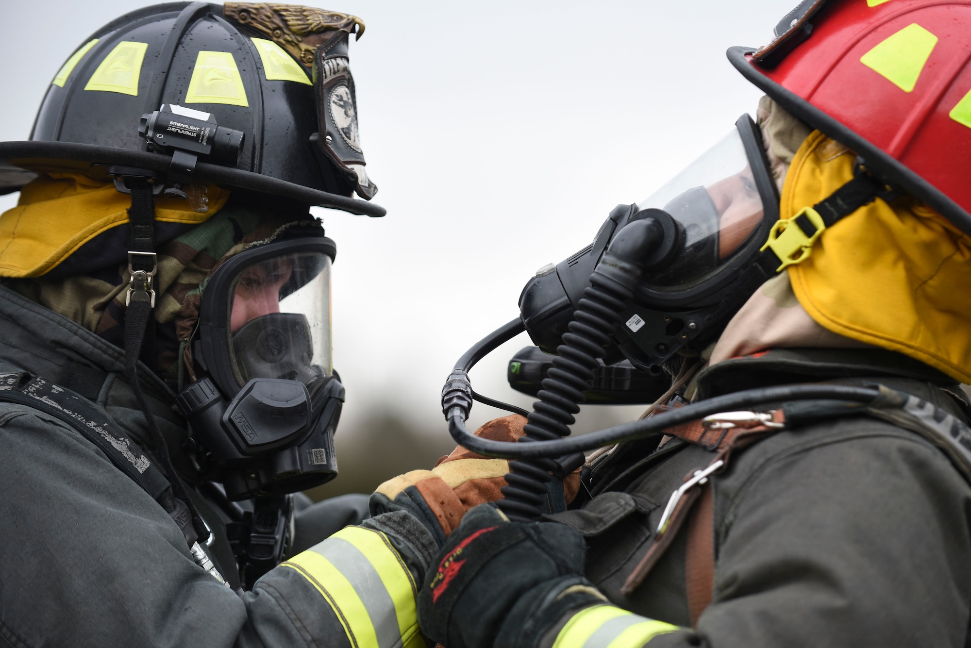 Two male firefighters make adjustments to their equipment