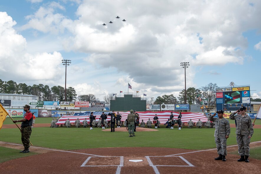 Nearly 50 Airmen attending James C. Binnicker Airman Leadership School at Seymour Johnson Air Force Base, North Carolina, hold the flag Feb. 24, 2018, while four F-15E Strike Eagles fly over Grainger Stadium in Kinston, North Carolina, during the national anthem before game two of the Freedom Classic baseball tournament. The Freedom Classic is the annual tournament between the Air Force and Naval Academy baseball teams, which has been held in Kinston for the past eight years. (U.S. Air Force photo by Tech. Sgt. David W. Carbajal)