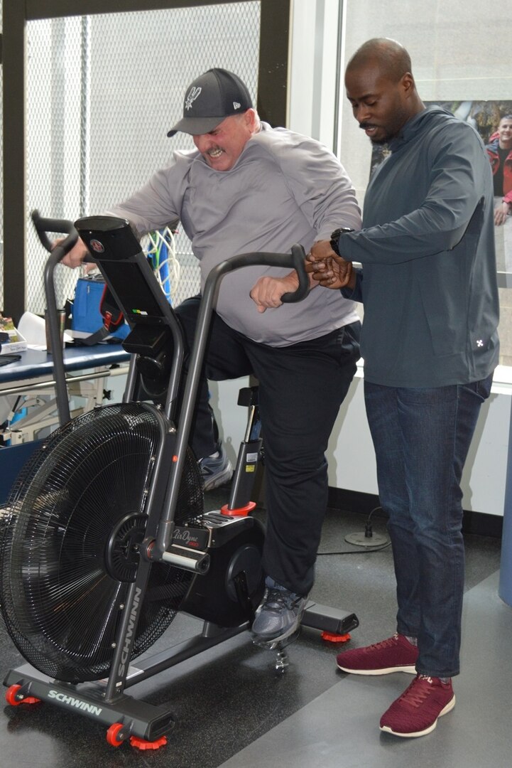 David Colbath completes a workout on an exercise bike Feb. 2, 2018 at the Center for the Intrepid at Joint Base San Antonio-Fort Sam Houston as physical therapist Oluwasegun Olomojobi times him. Colbath is one of eight people who were brought to Brooke Army Medical Center with multiple gunshot wounds inflicted by a lone gunman in Sutherland Springs, Texas on Nov. 5, 2017. He is currently rehabilitating from his injuries at the CFI.