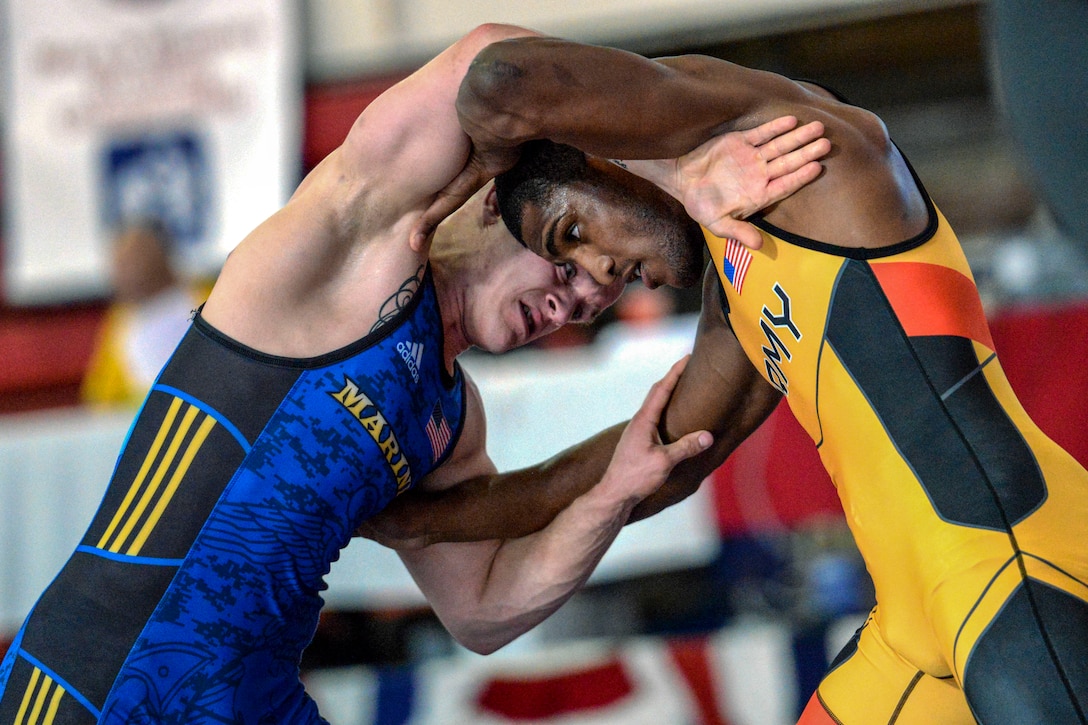 Two wrestlers lean into each other with their heads touching an arms forming an "O" around their heads and torsos.