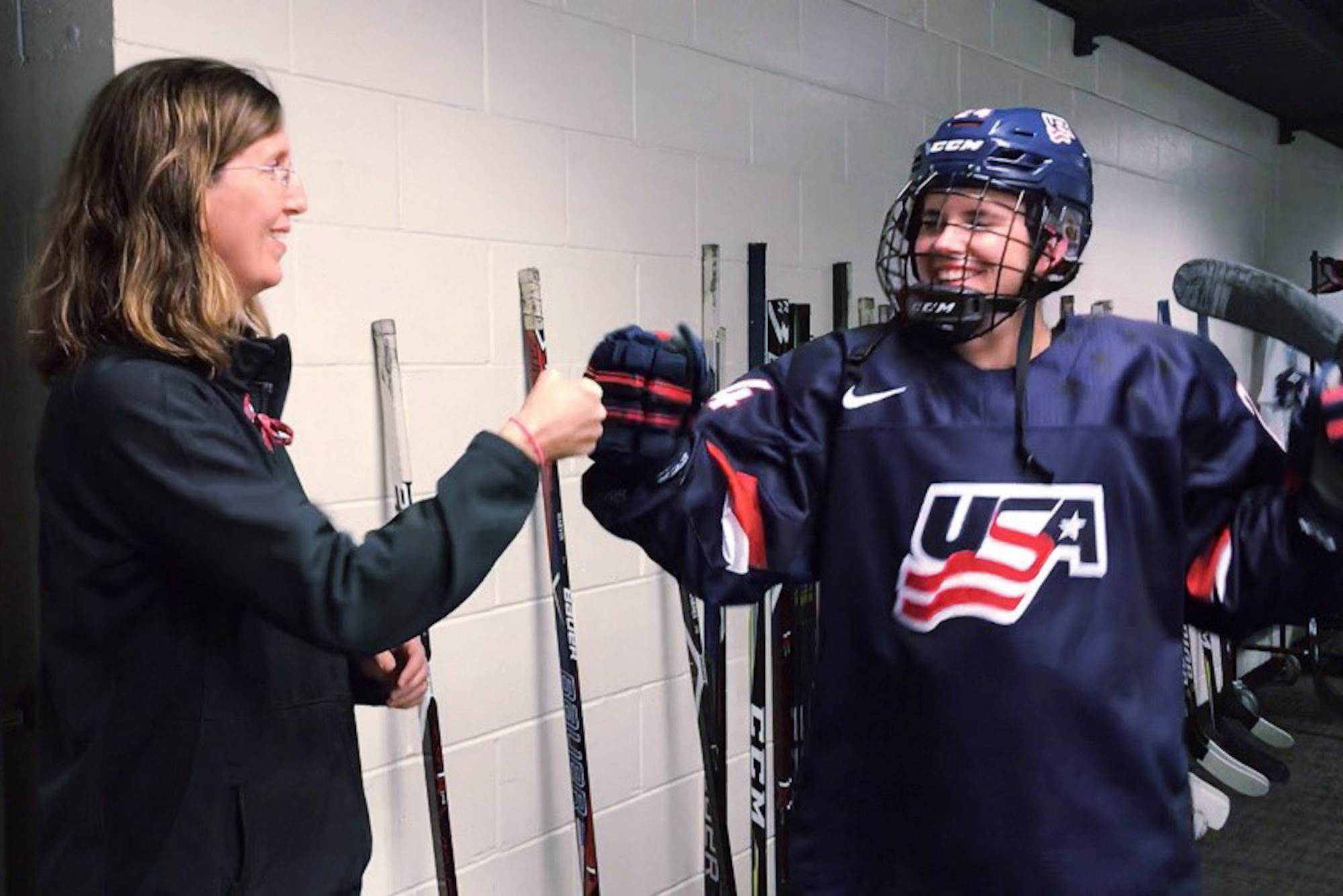 A woman fist bumps a female hockey player.