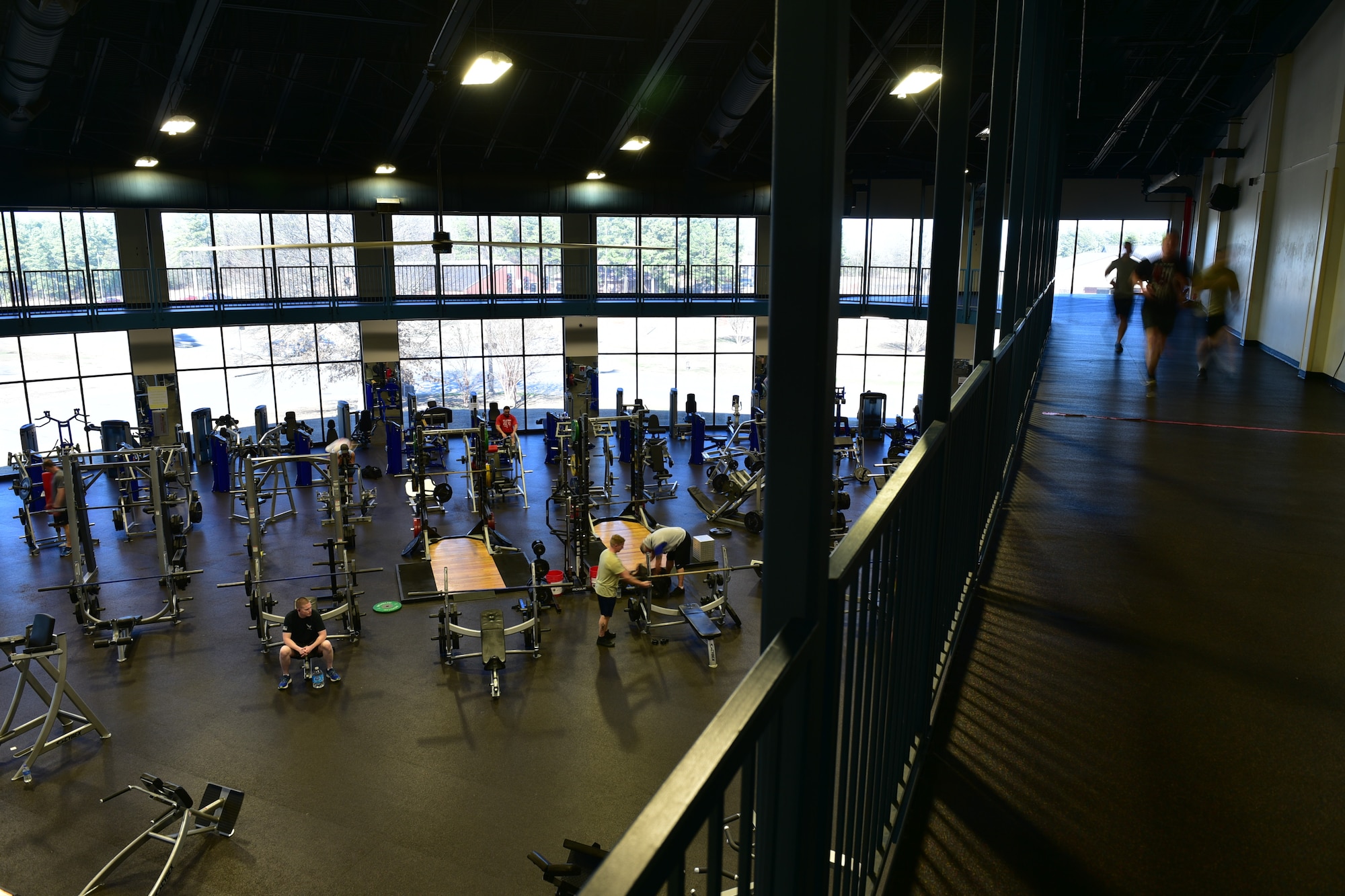 Airmen run on a track above a weight room.