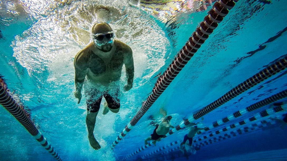 Service members and veterans compete in a freestyle swimming event in a pool.