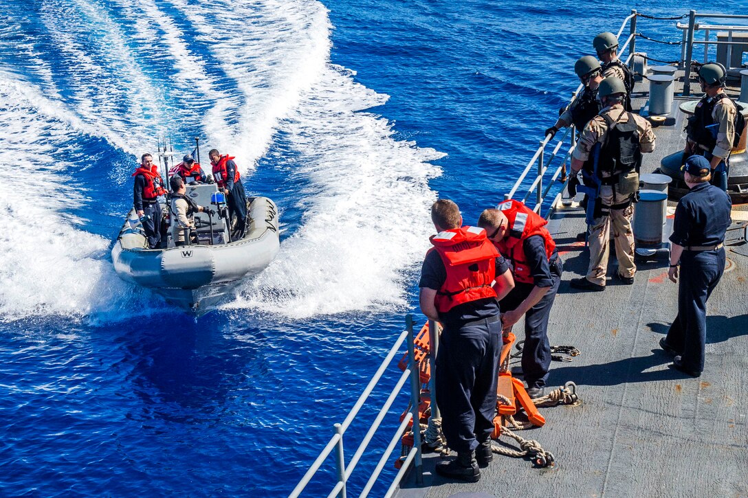 Sailors in a rigid hull inflatable boat pull alongside Ticonderoga-class guided-missile cruiser USS Lake Champlain.