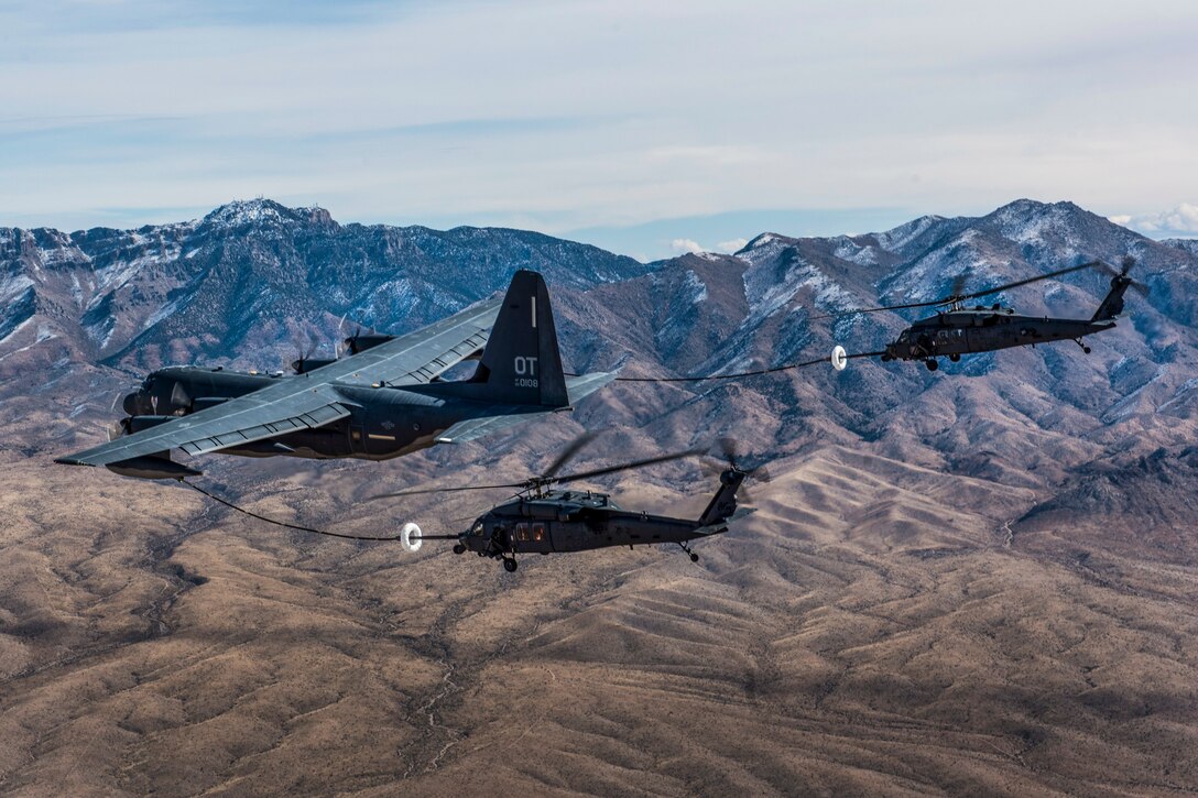 Two military helicopters receive fuel from a military cargo aircraft while flying.