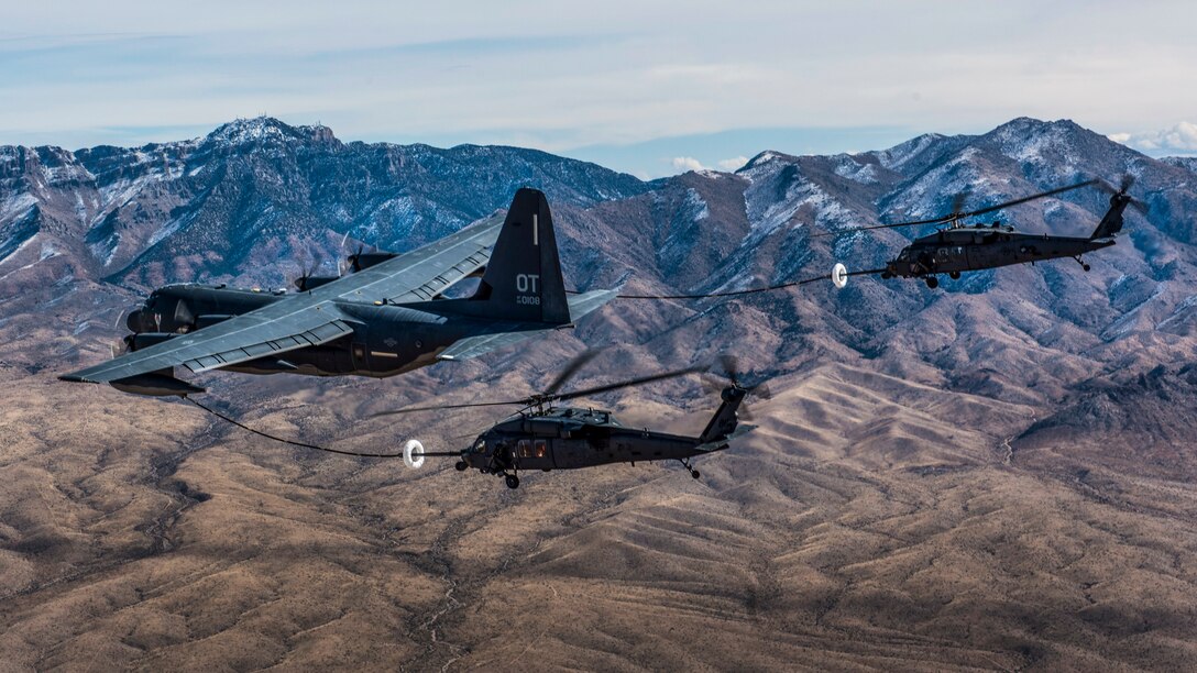 Two military helicopters receive fuel from a military cargo aircraft while flying.