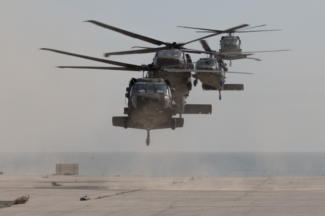 Four military helicopters prepare to land at a base in Kuwait.