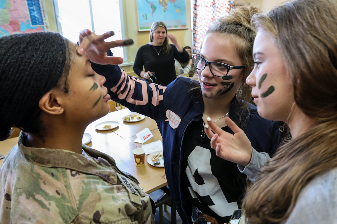 Two students apply camouflage paint to a soldier's face.