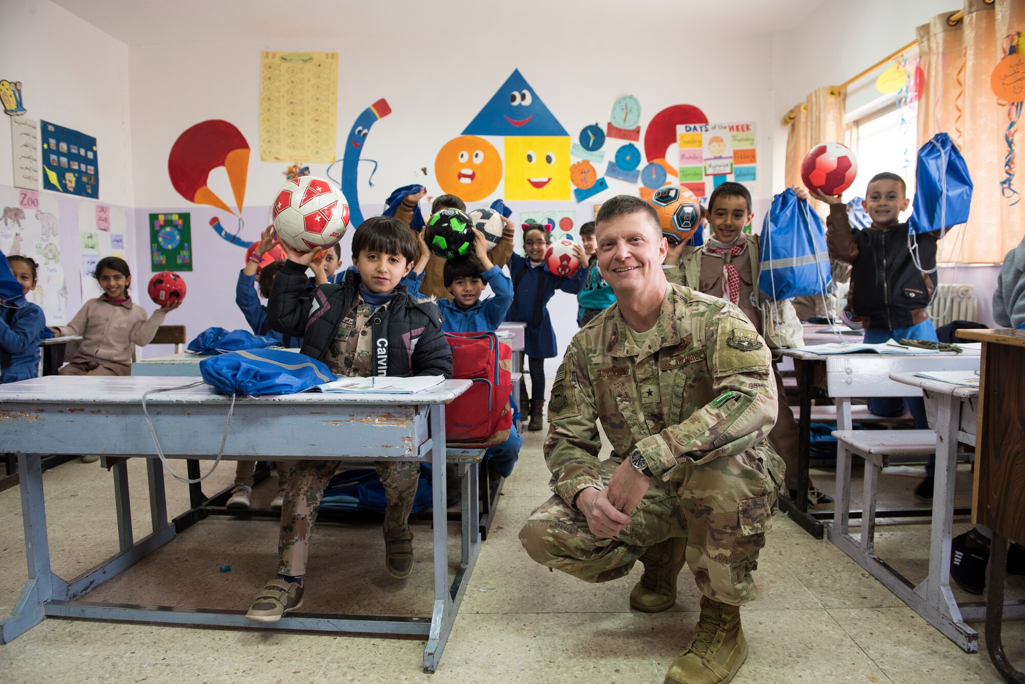 U.S. Air Force Brig. Gen. Kyle Robinson, 332d Air Expeditionary Wing commander, poses with school children during a donation drop-off February 26, 2018, at an undisclosed location. The project, named, “Care for Kids,” was a combined effort between service members and their friends and family back home, with the goal of providing school and sports equipment to two schools and a refugee camp. (U.S. Air Force photo by Staff Sgt. Joshua Kleinholz
