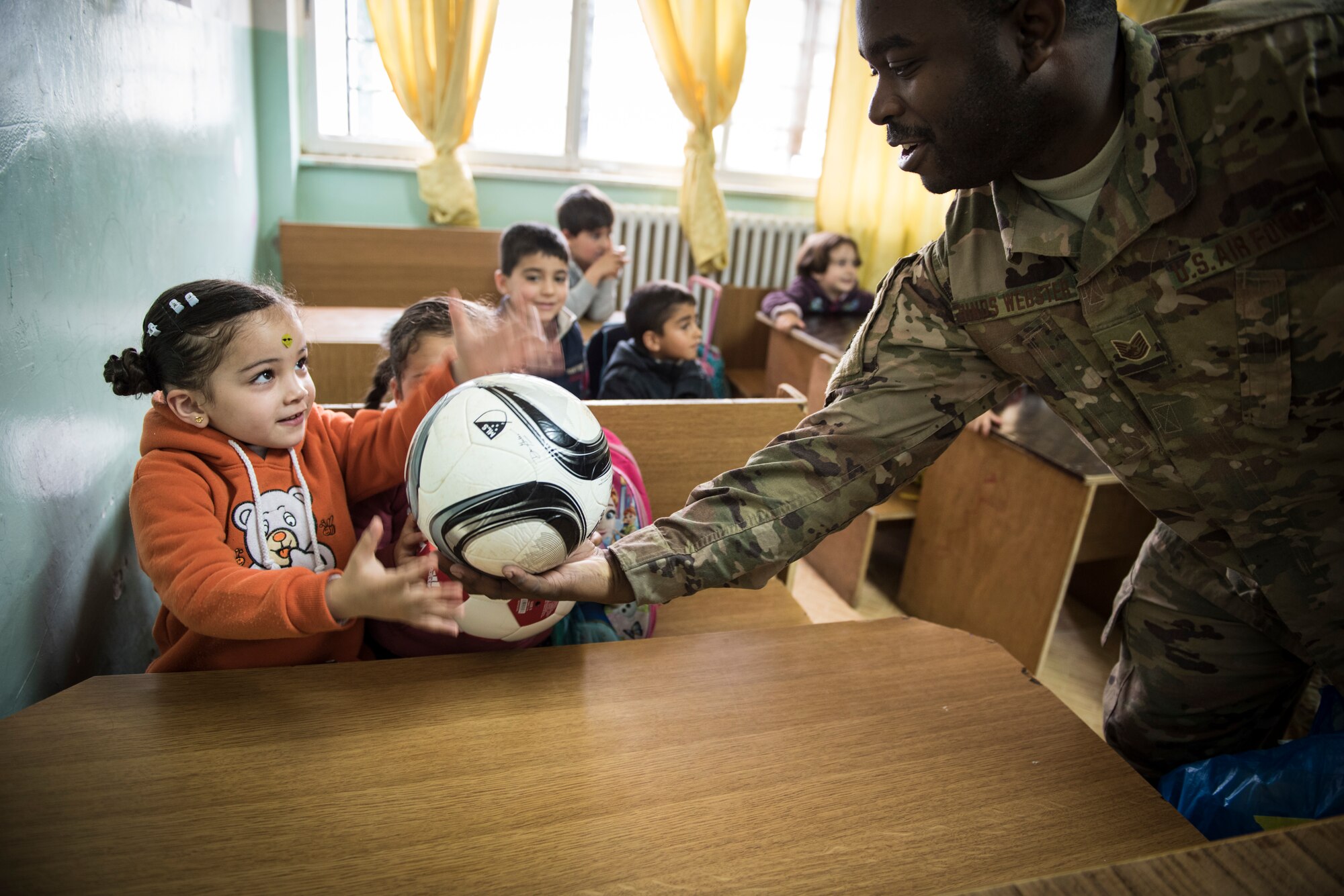 Tech. Sgt. Darren Hinds-Webster, assigned to the 332d Mission Support Group, hands out soccer balls to school children during a donation drop-off February 26, 2018, at an undisclosed location. Service members reached out to family and friends back home and were able to provide school supplies and soccer balls to two local schools, as well as clothing, books, and hygiene products for refugees in the region. (U.S. Air Force photo by Staff Sgt. Joshua Kleinholz)