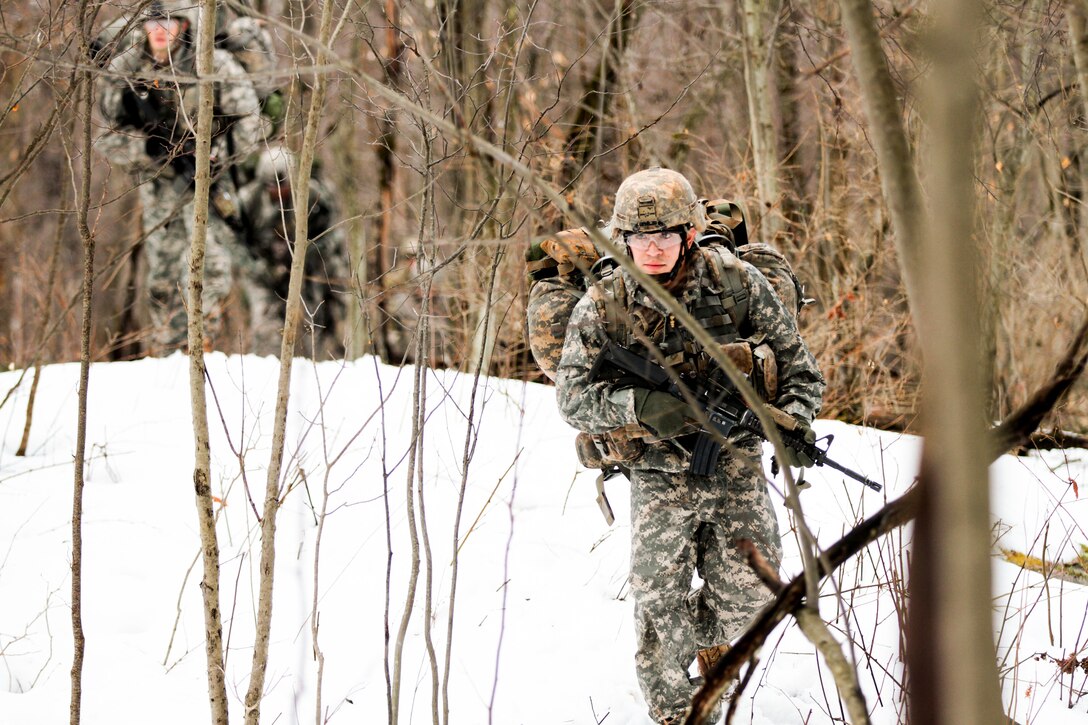 Soldiers move through heavily wooded terrain and snow.