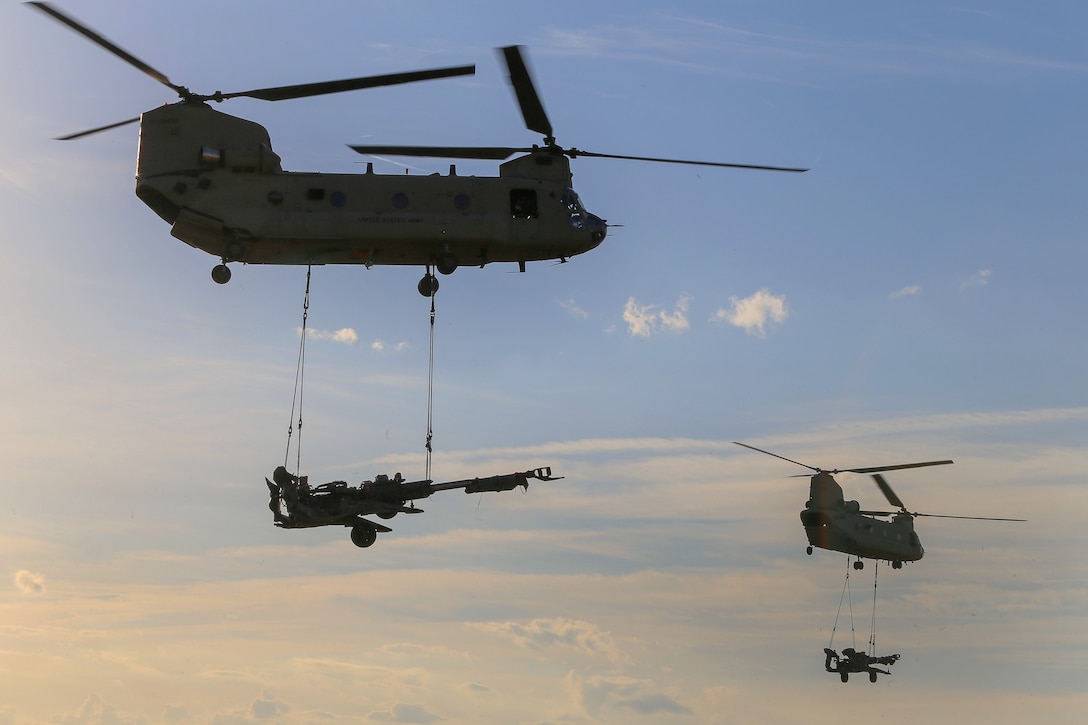 Two CH-47 Chinook helicopters sling-load M777A2 howitzers.