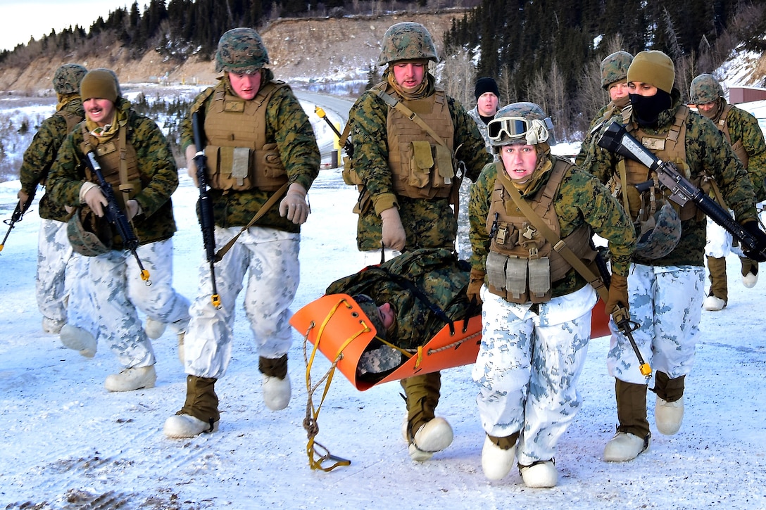 Marines in cold-weather gear carry a mock patient in an orange stretcher.