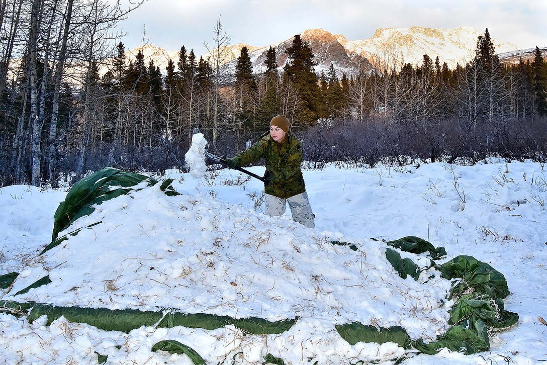 A Marine adds snow covering a newly constructed thermal shelter.