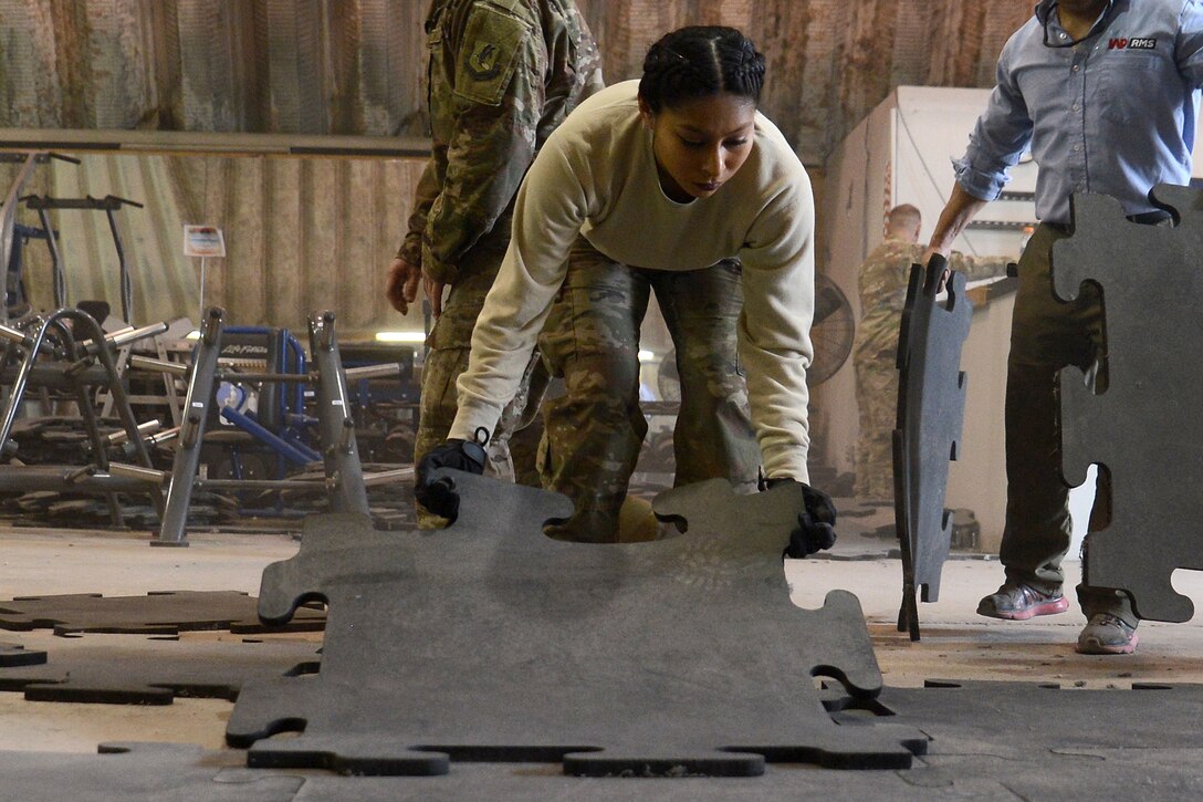 An airman lays down flooring at a fitness center.