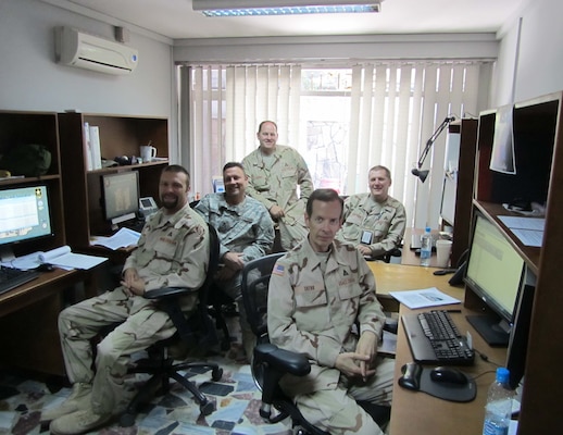 Steve Zeltner, seated on desk in front of the window, stood up the original TAD-Afghanistan Programs Team in summer 2012 in Kabul Afghanistan. With him are program managers, from left, Aaron Hoover, Dan Echols, Mike Costello, and Ray Tatro. He leaves a legacy of customer service in the U.S. Central Command area of operations as he retires from the Transatlantic Division.