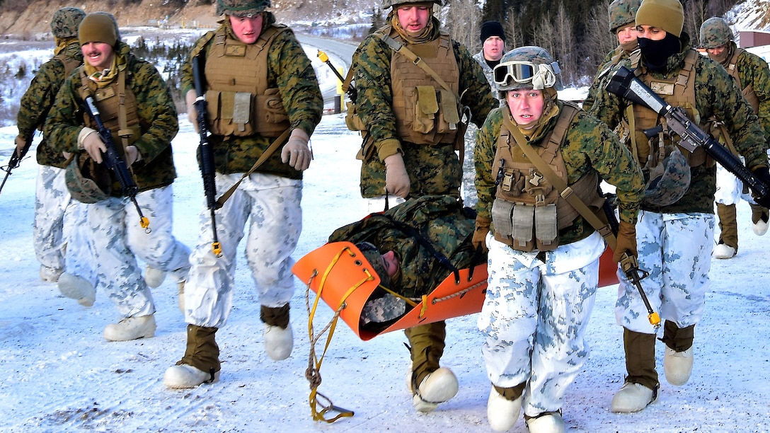 Marines in cold-weather gear carry a mock patient in an orange stretcher.