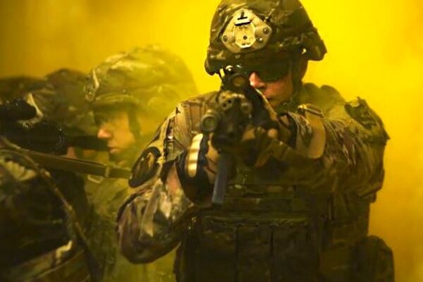 An airman holds a rifle while surrounded by yellow smoke.