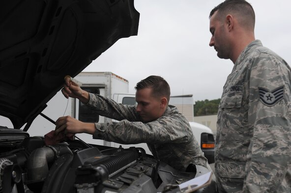 Man checks oil of Government Vehicle as Supervisor inspects work.
