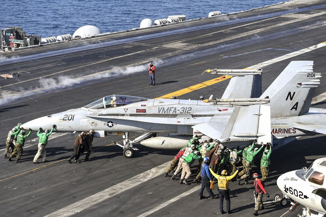 Sailors move a Hornet on the flight deck of an aircraft carrier.