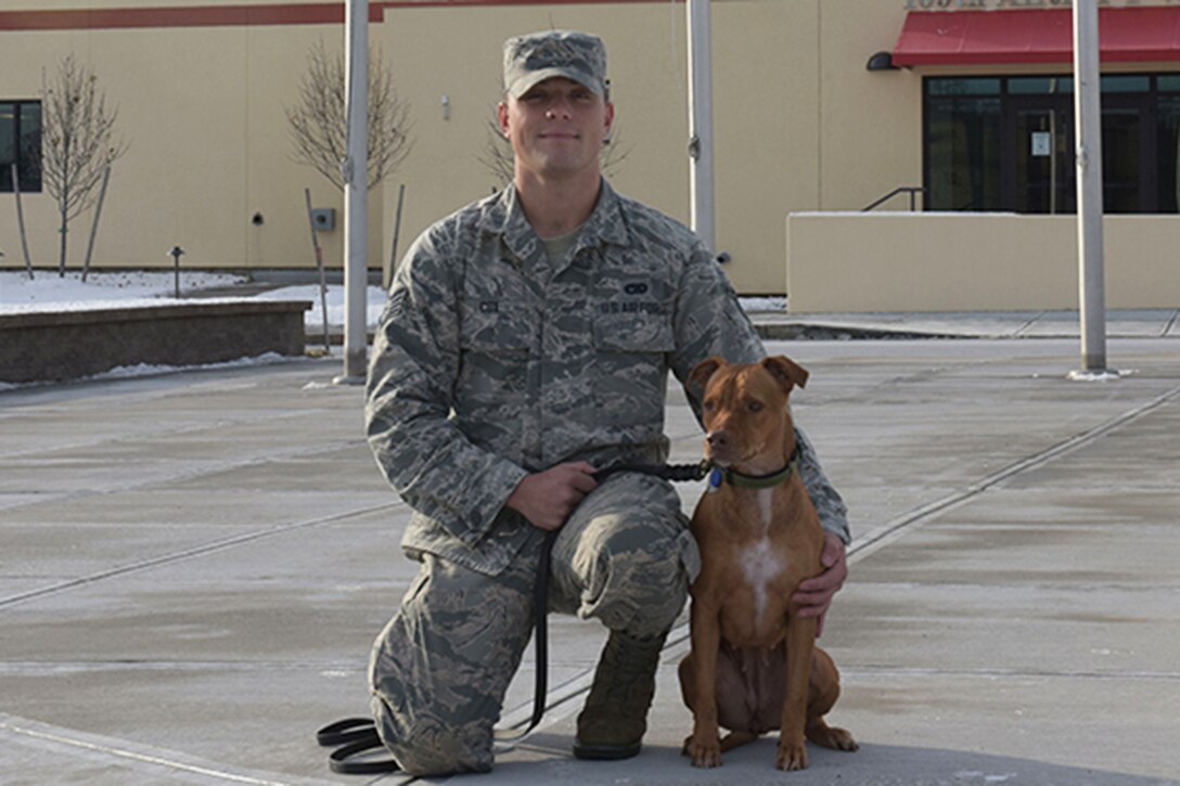 An airman kneels next to his dog at an air base.
