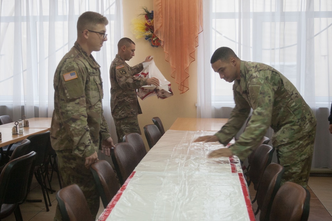 Three soldiers cover a long table with a tablecloth.
