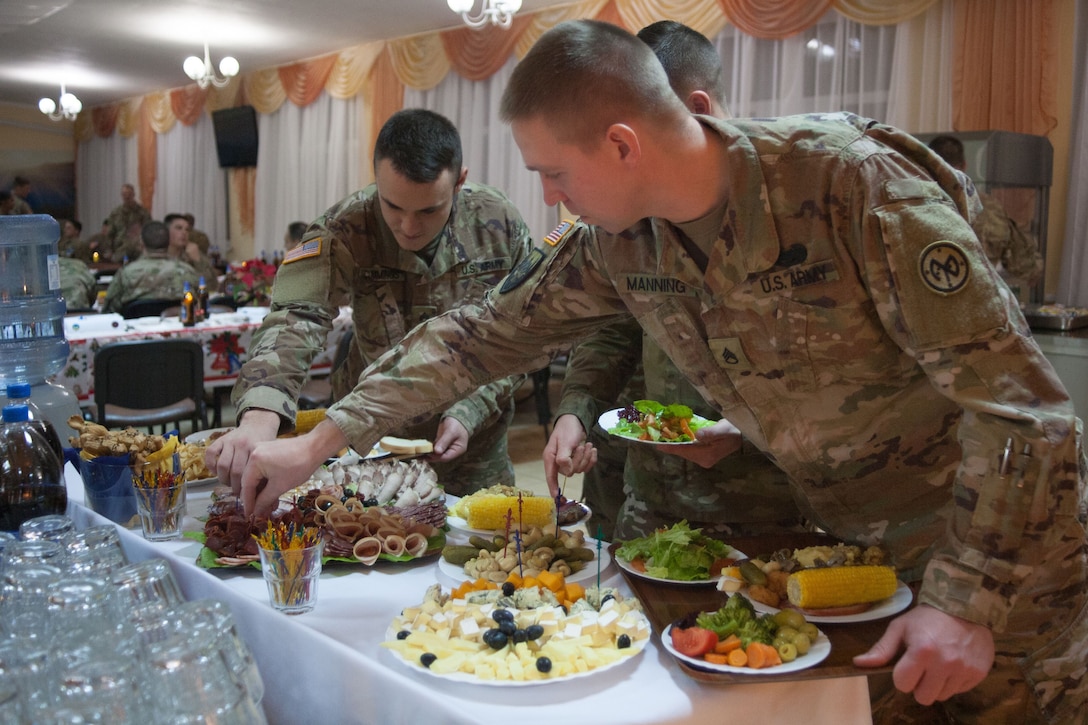 Soldiers standing at a table fill several plates with Christmas dinner.