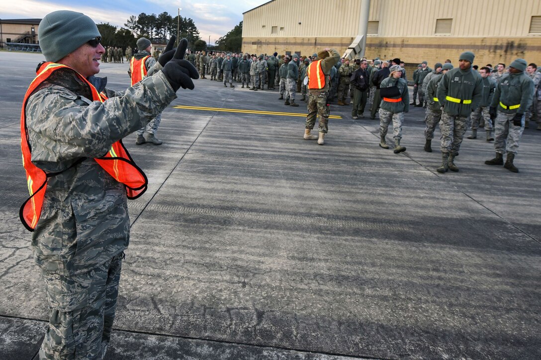 An airman makes a signal with his hands as other airmen walk down a  runway.