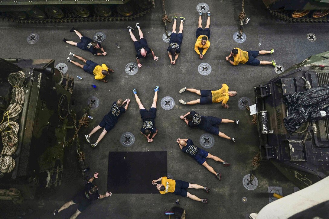 Sailors, seen from overhead, lie on a ship's floor in workout gear.