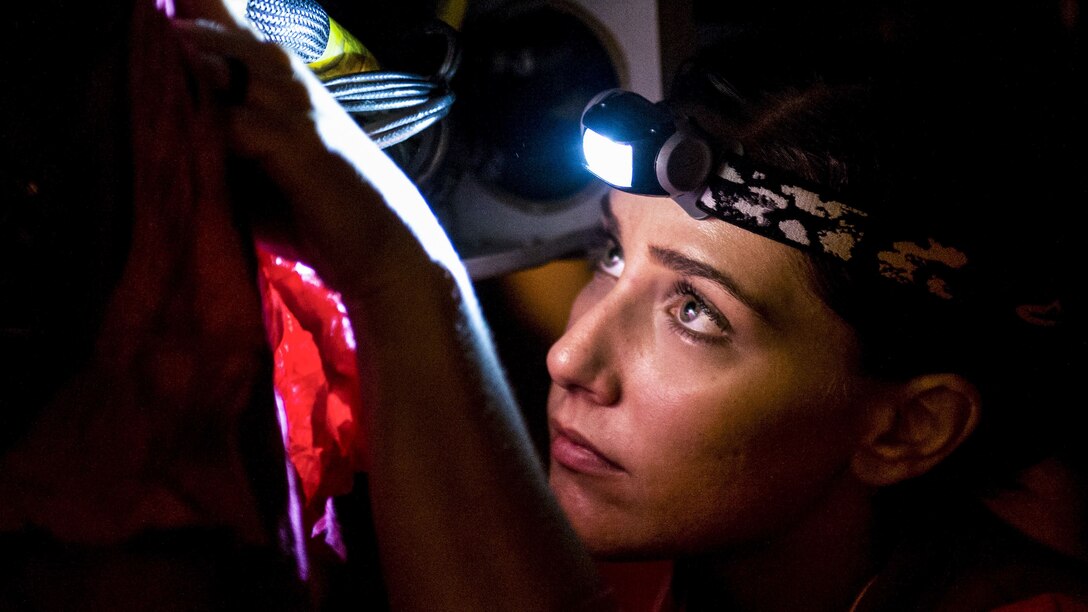 A sailor wearing a headlamp looks up and works on something with her hands.