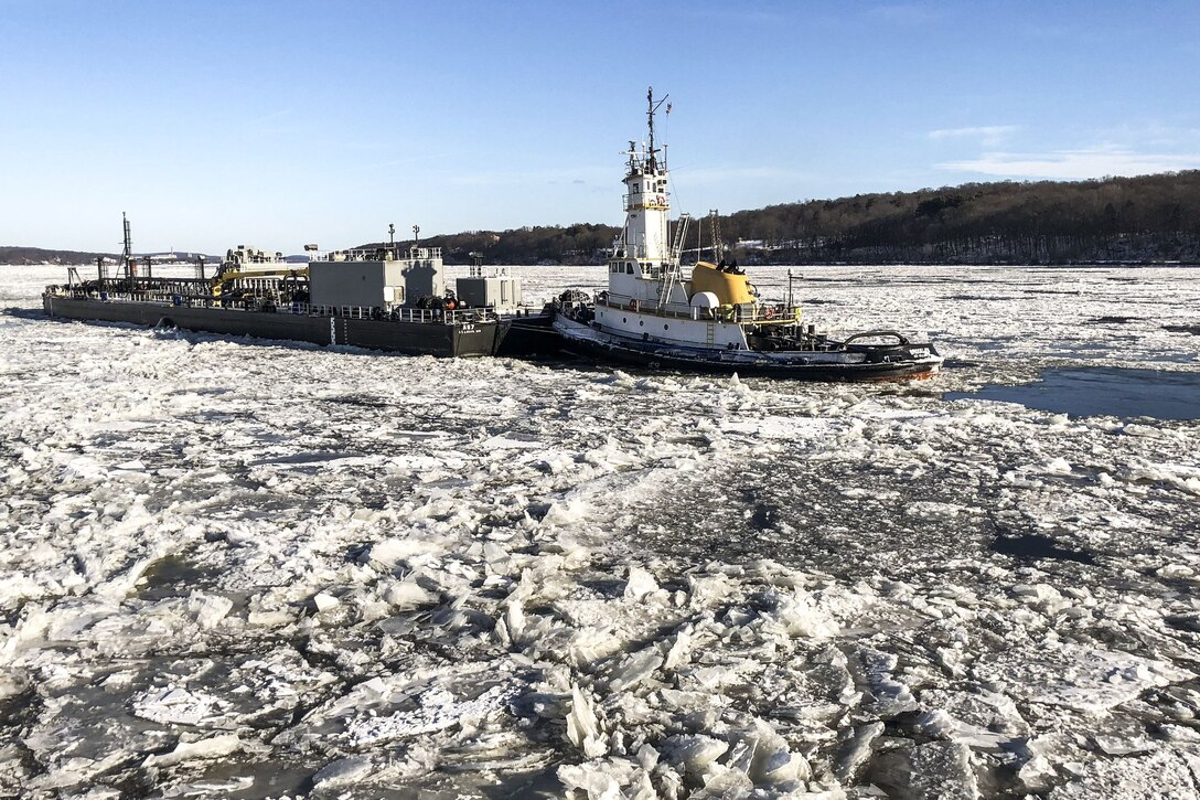 A Coast Guard cutter operates next to a tugboat amid ice-covered water.