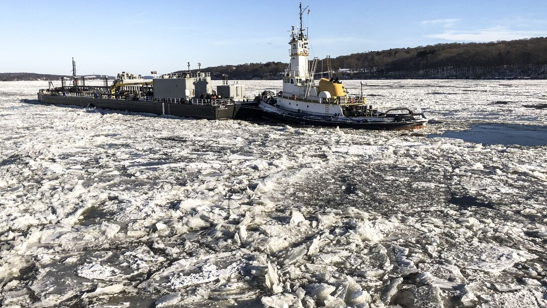 A Coast Guard cutter operates next to a tugboat amid ice-covered water.