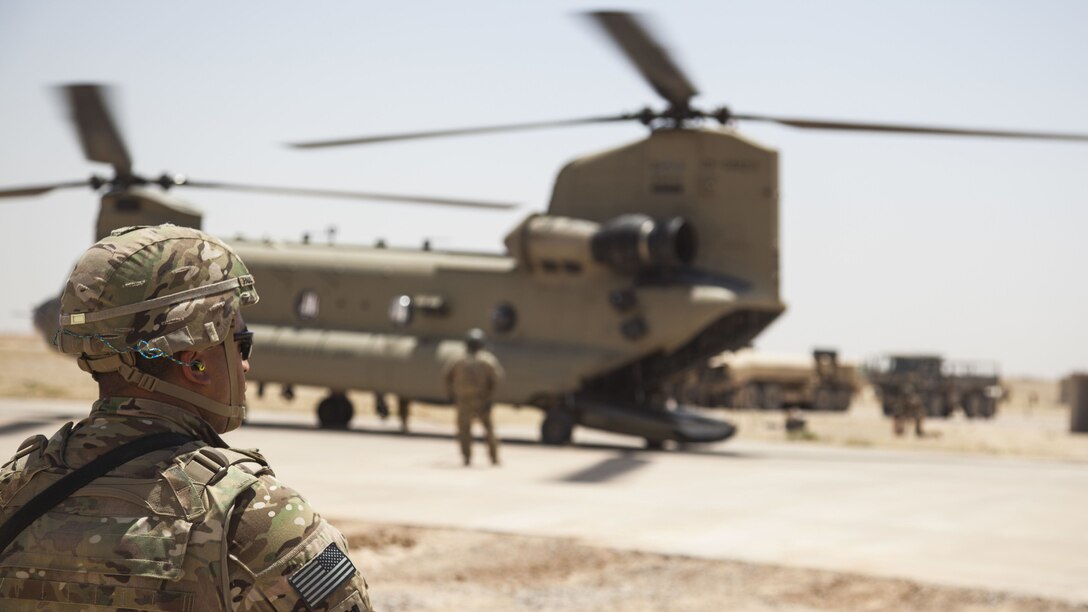 A soldier stands in front of a  CH-47 Chinook being refueled.