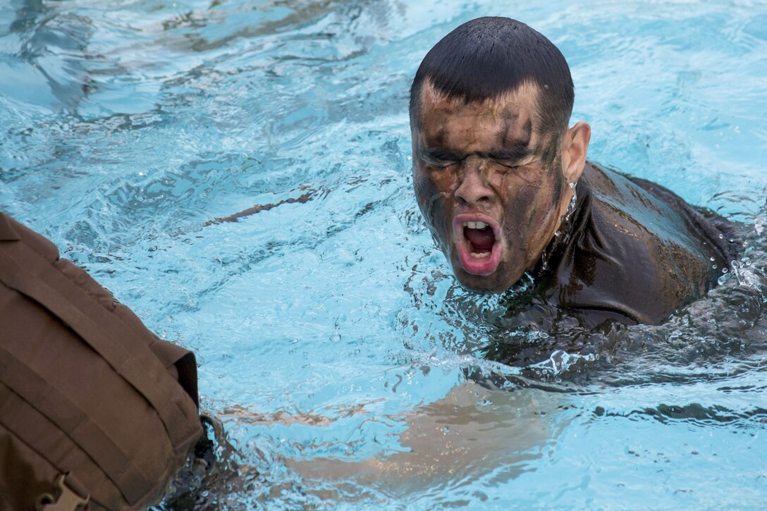 A Marine wearing face paint a tan shirt takes a breath while swimming in a pool.