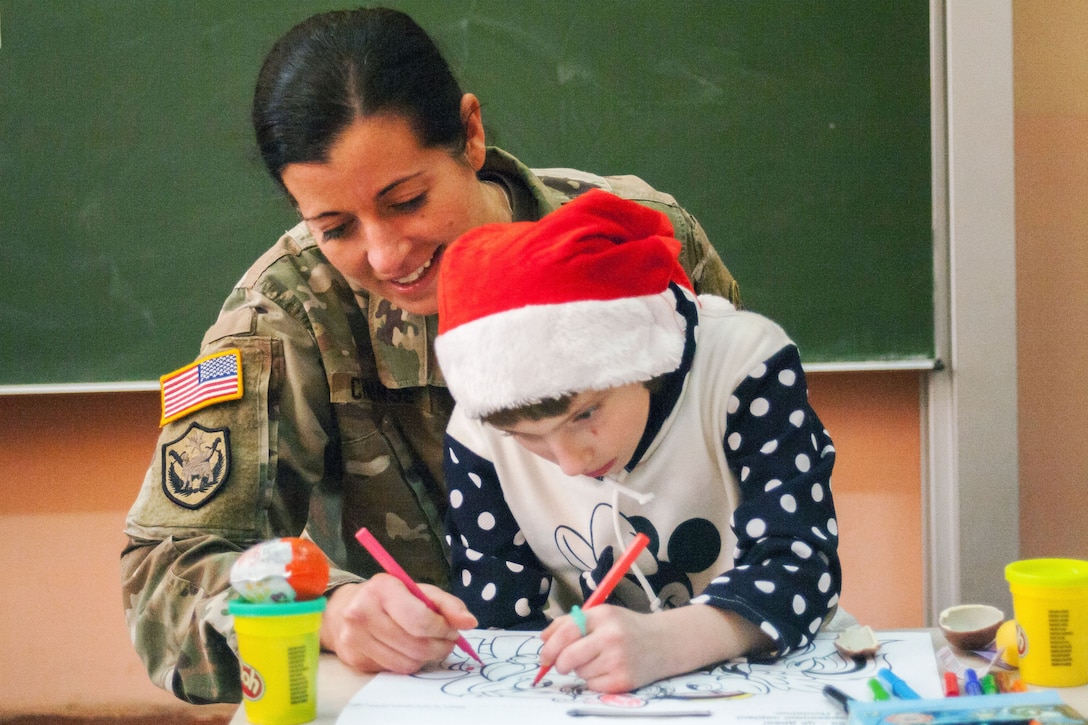 A soldier helps a child color a picture.