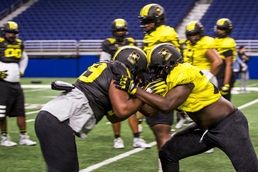 Two football players butt helmets while leaning into each other on a playing field.