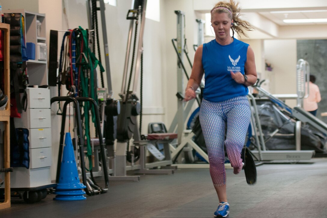 A woman with a prosthetic leg runs on an indoor track.